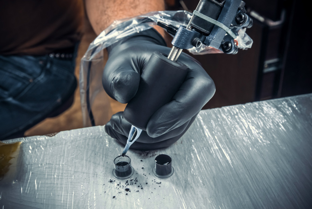 A tattoo artist dipping his needle in black ink in the parlor