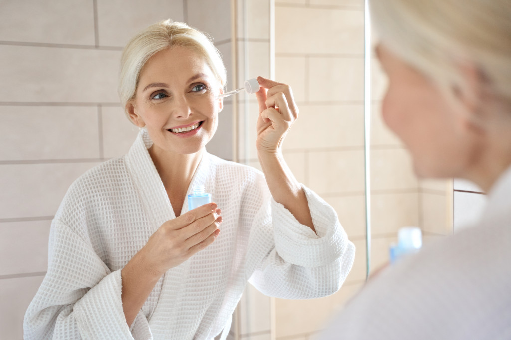 A mature woman applying serum while looking at a mirror