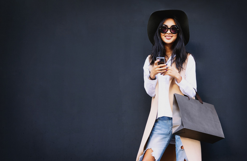 Young woman smiling while using her phone and carrying a bag.